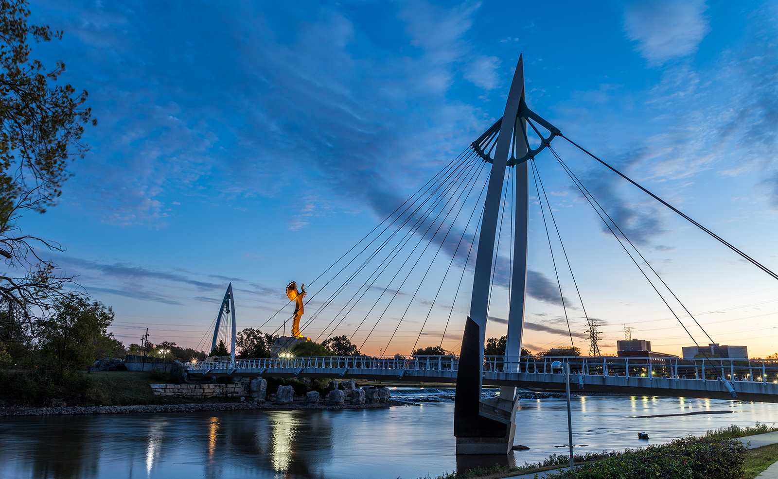 A nighttime view of a bridge over a river, with the city skyline in the background and a bridge walkway.