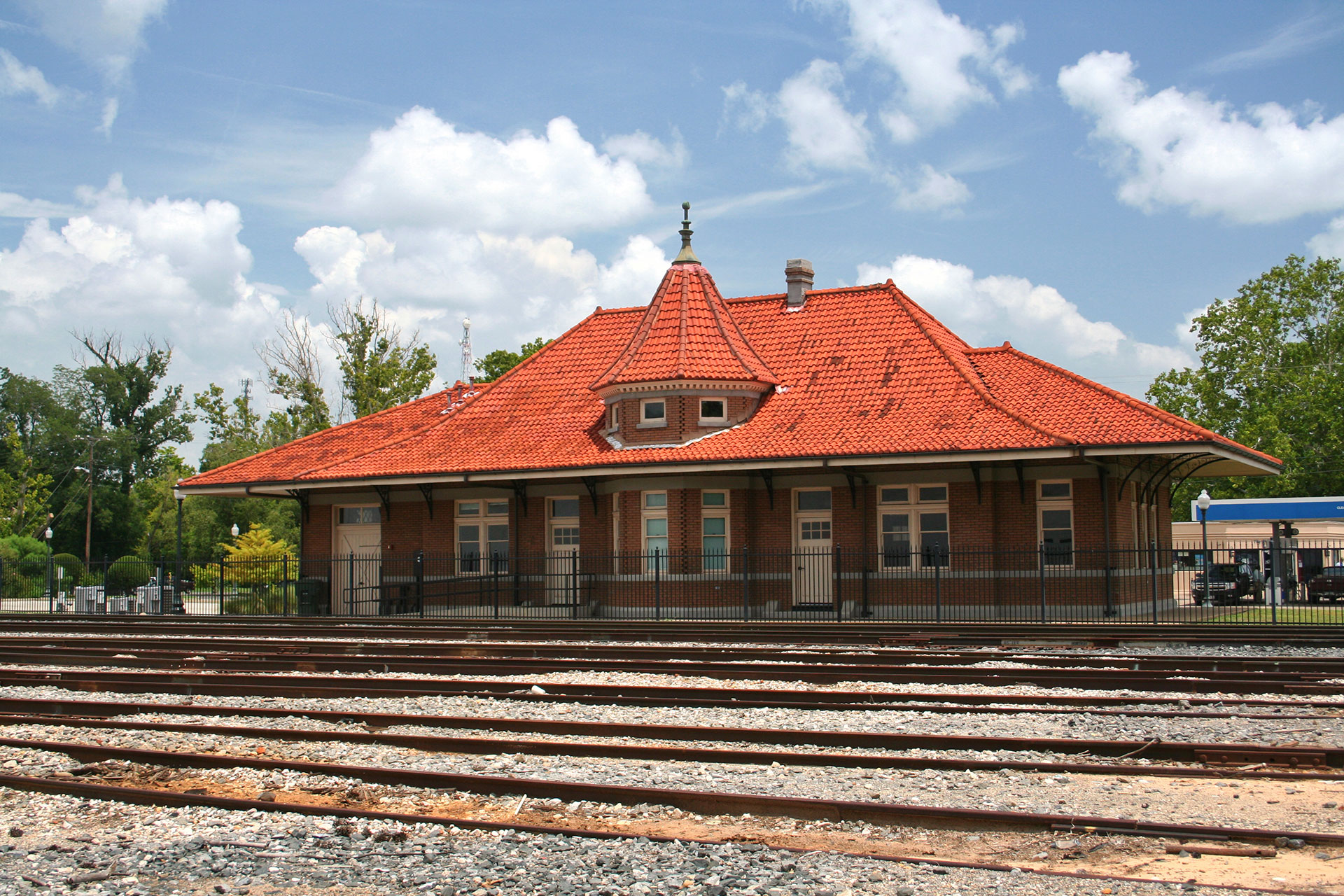 An old-fashioned train station with a red roof, situated on railroad tracks.