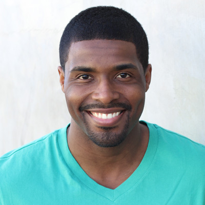 The image shows an elderly couple sitting close together, with the man on the left and the woman on the right. They appear to be enjoying a moment of happiness or affection, as indicated by their smiles and the way they are positioned towards each other. The setting seems to be outdoors during daylight, possibly in a park or garden, given the presence of greenery in the background.