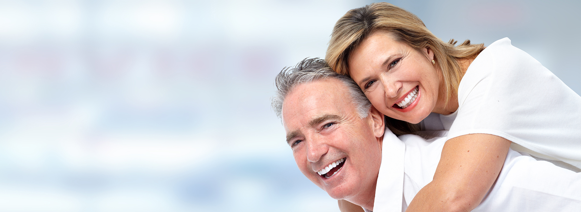 The image shows a man and a woman embracing each other, with the woman smiling and both appearing to be in a happy or content mood. They are dressed in casual attire and appear to be middle-aged adults.