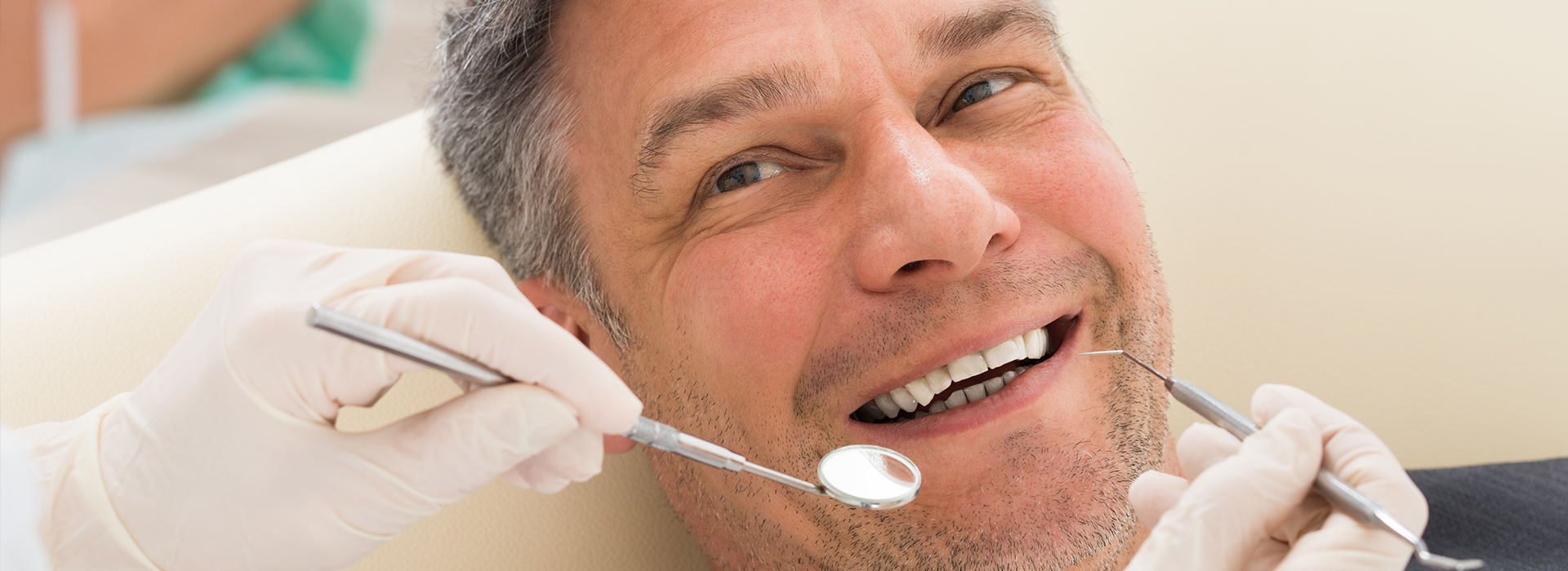 A man is sitting in a dental chair, smiling at the camera while receiving dental care.