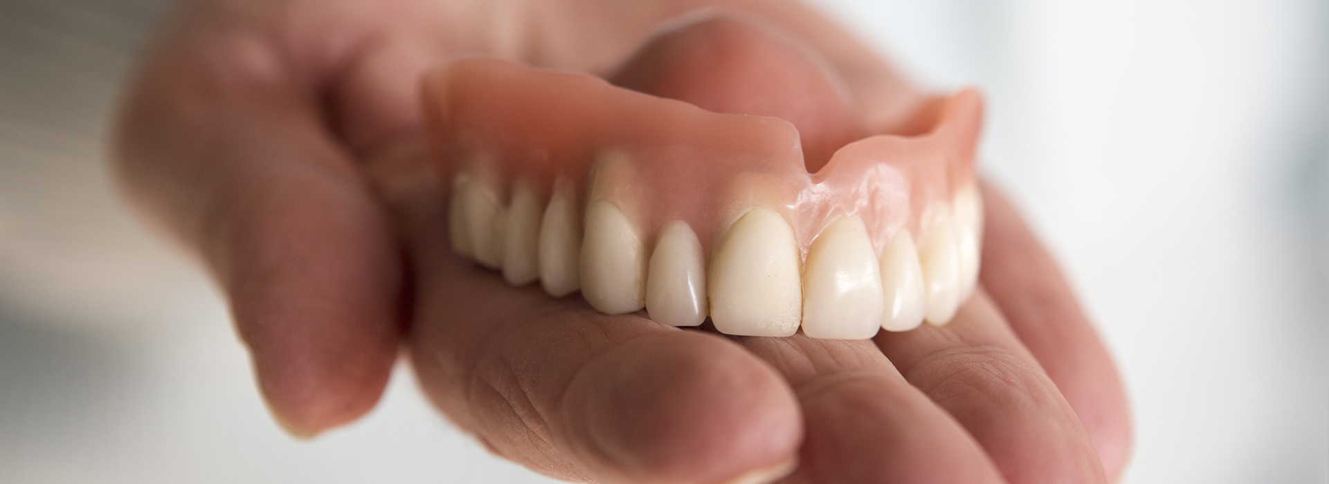 The image shows a person s hand holding an upper denture with multiple teeth.