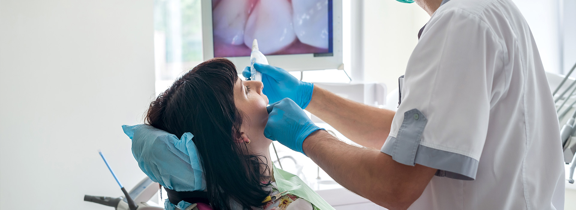 A dental professional performing a procedure on a patient s mouth, with medical equipment and the patient wearing a protective mask.