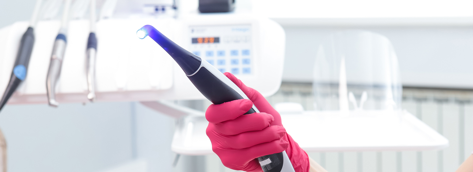 A person in a pink glove holding an electronic device near a machine, likely in a laboratory or medical setting.