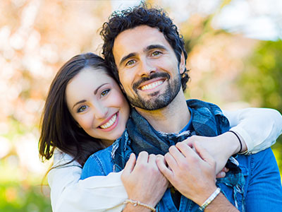 A man and a woman, both smiling, embrace in a warm hug.