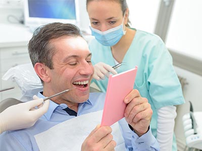 A smiling man holding a pink card, surrounded by dental professionals in a clinical setting.