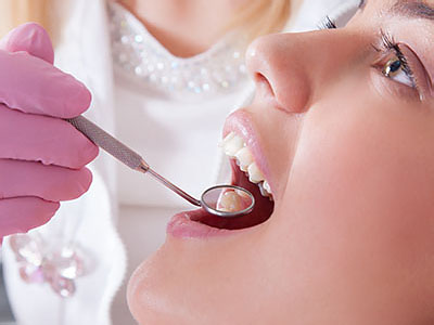 A dental professional in a white coat and purple gloves is performing oral care on a person s teeth using specialized equipment.