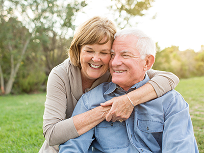 An elderly couple embracing and smiling, with the man wearing a blue shirt and the woman in a white top.