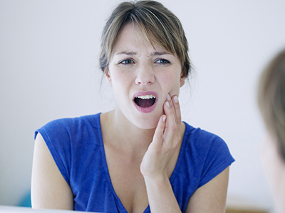 A woman with her mouth open, looking upwards and to the left, while holding a toothbrush near her mouth.