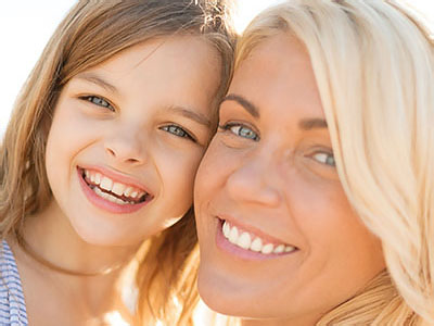 A woman and a young girl smiling at the camera, sharing a joyful moment together.