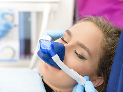 A person receiving medical treatment, with a blue oxygen mask over their nose and mouth, while being attended to by a healthcare professional.