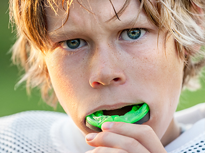 A young male athlete, with blonde hair and a serious expression, holding a green mouthguard in his hand.