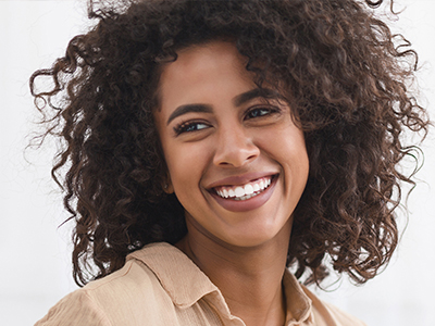 The image features a smiling individual with curly hair, wearing a light-colored top, against a plain background.