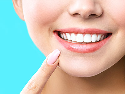 A close-up of a woman with a radiant smile, showcasing her teeth and the glossy pink manicure.